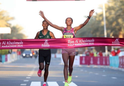 a woman running with a pink ribbon crossing the finish line